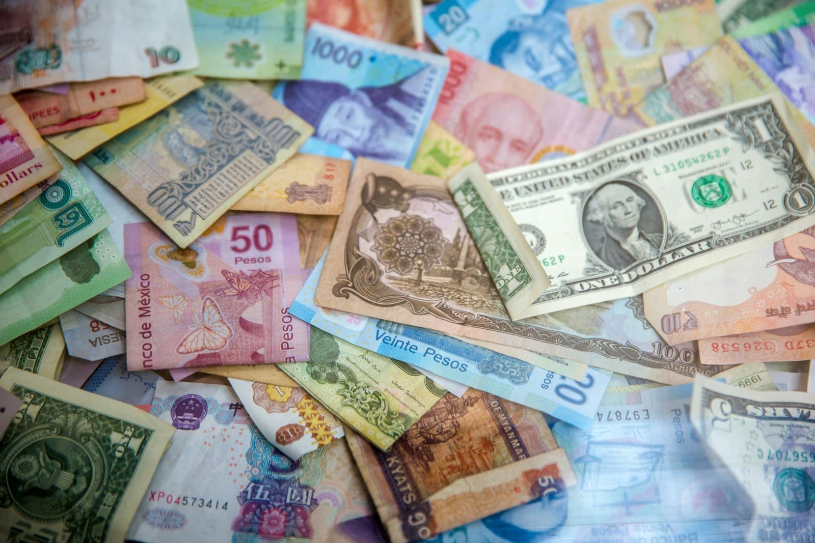 A pile of banknotes from several countries, including US dollars and Mexican pesos, spread across a table