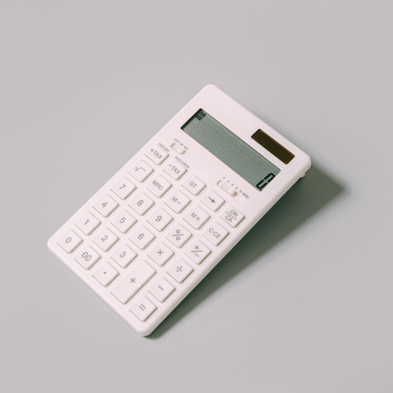 A white desk calculator lying at an angle on a plain light gray surface