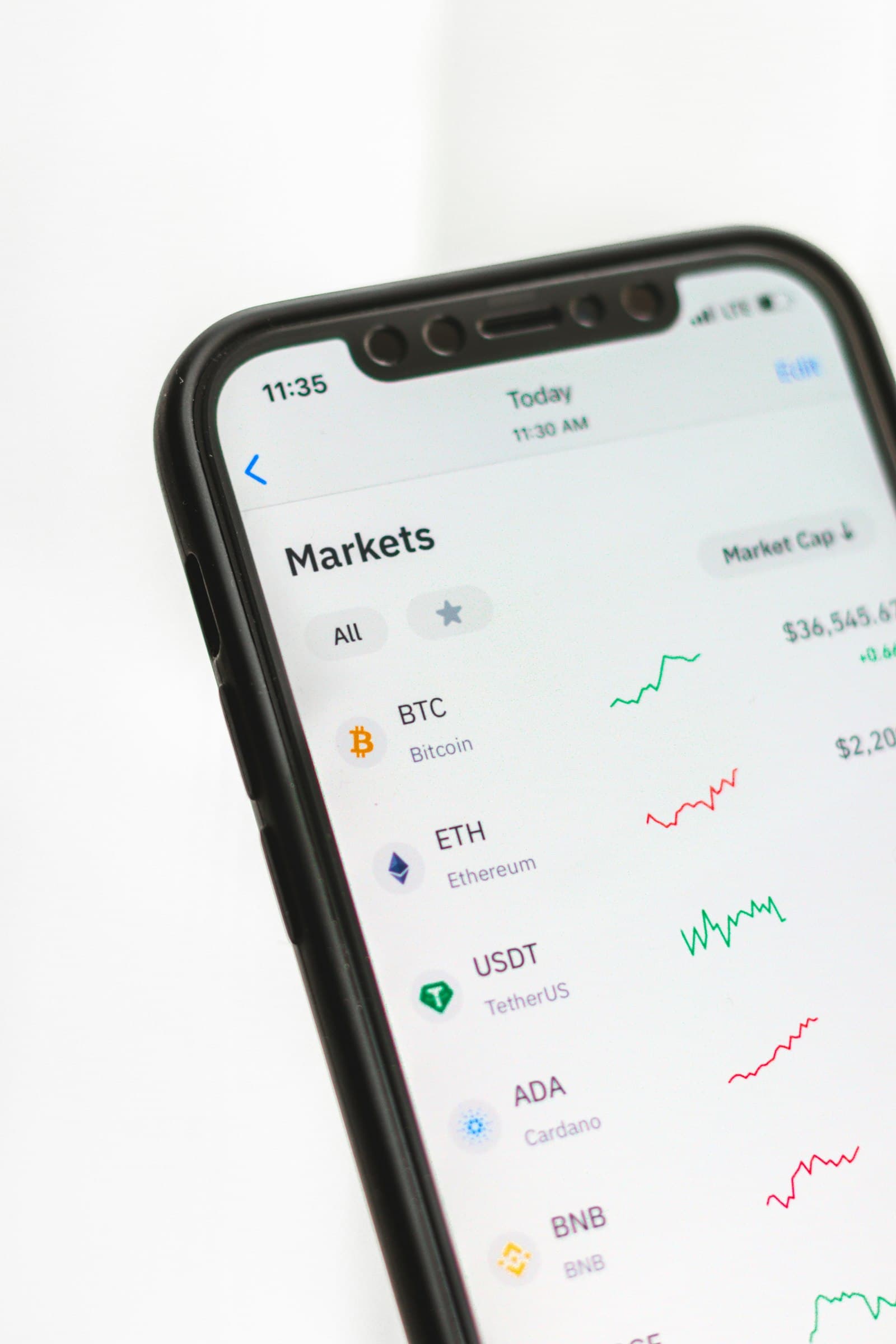 A phone showing a crypto markets list with Bitcoin and Ether prices and small charts